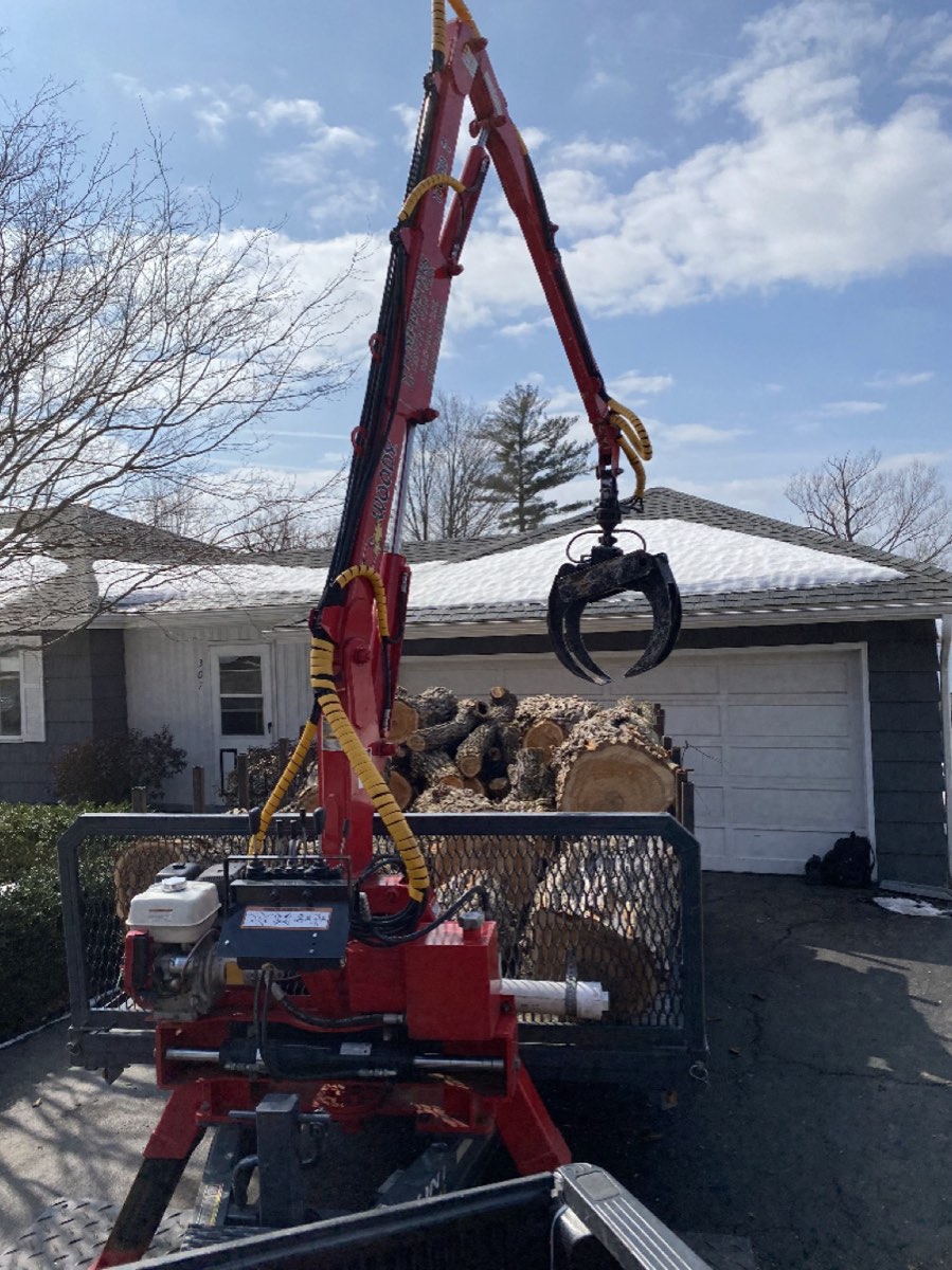 Grapple loader lifting logs onto a truck at a CNY home