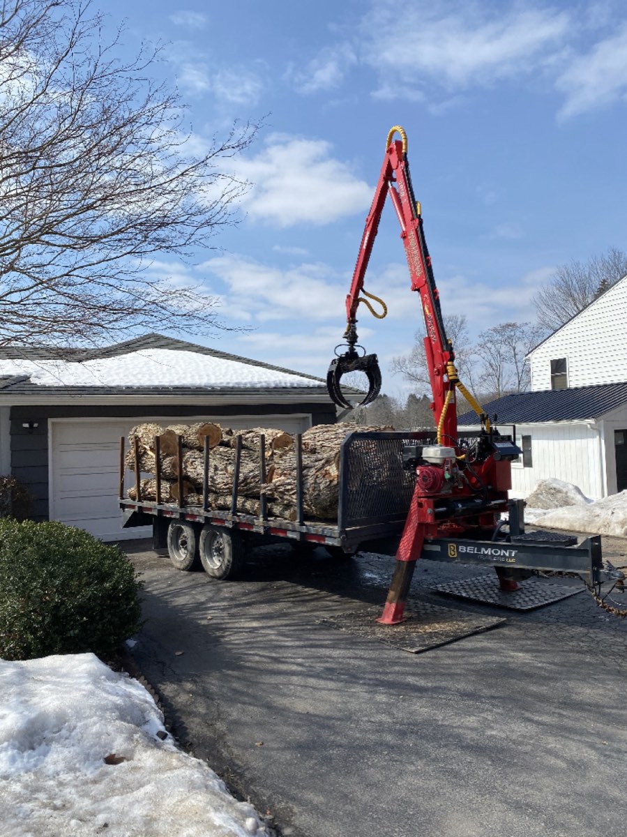 Red grapple loader stacking logs on a trailer at a CNY home
